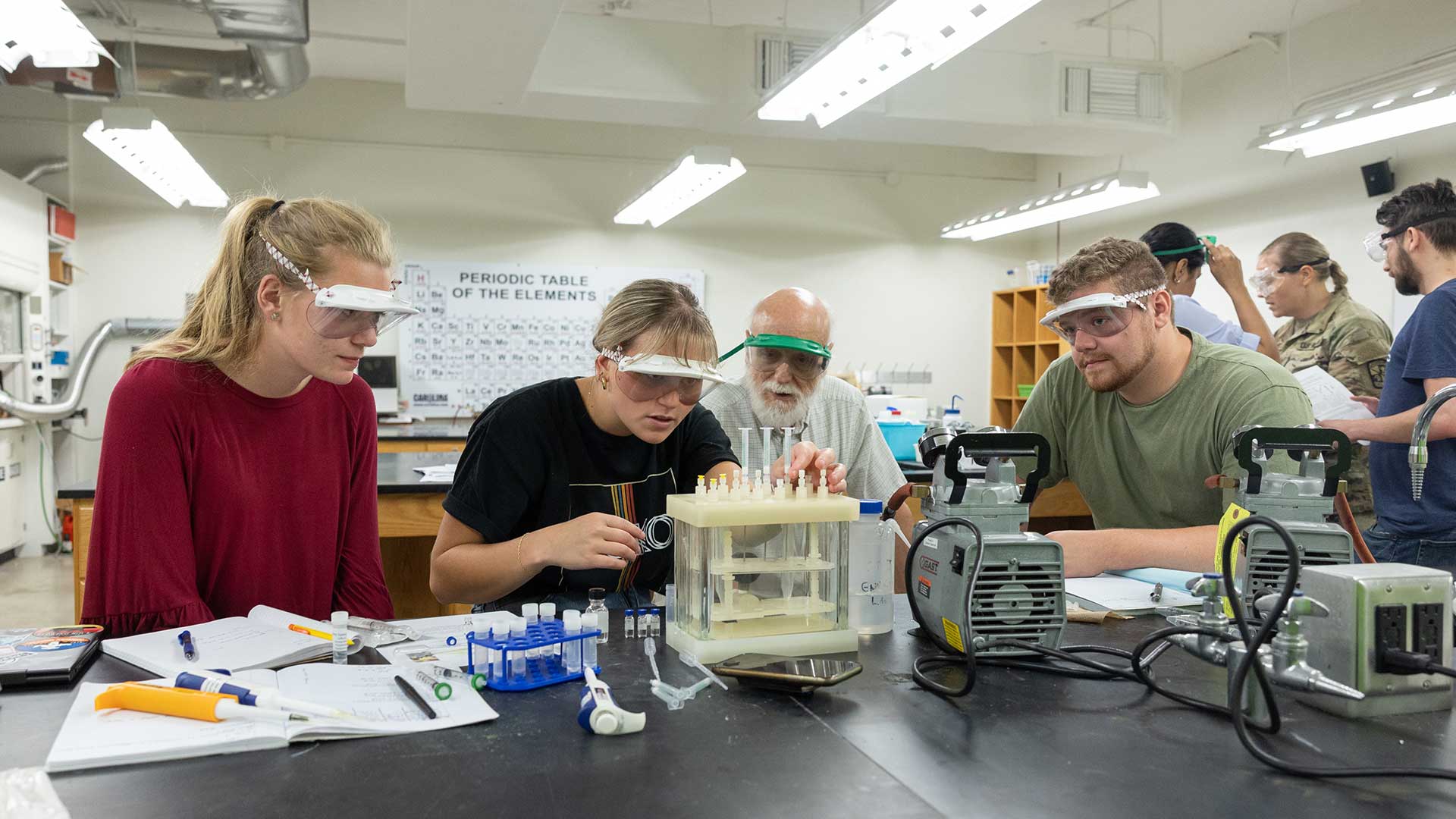 A group of chemistry students do prep work as a professor looks on.
