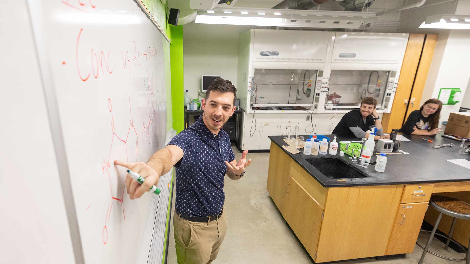 A chemistry teacher points to a dry erase board as he teaches class.