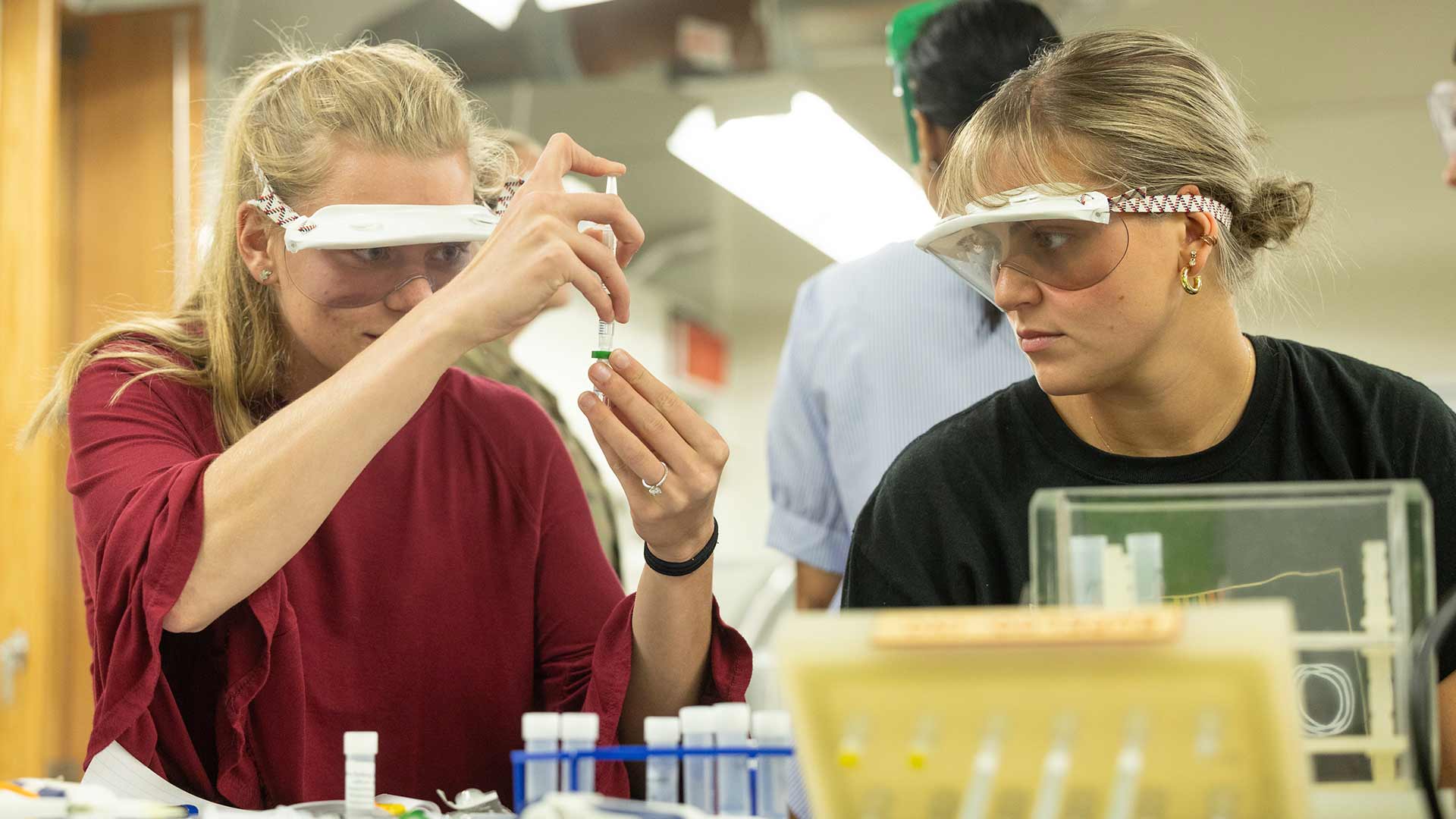 Two chemistry students handling materials in a lab setting.