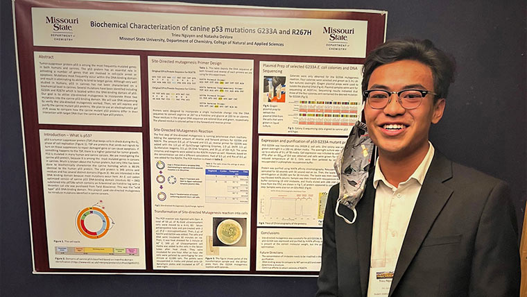 A chemistry student poses next to his research poster board during undergraduate research day.