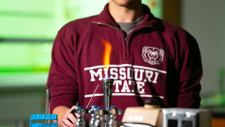 A chemistry student tests the flame from a bunsen burner.