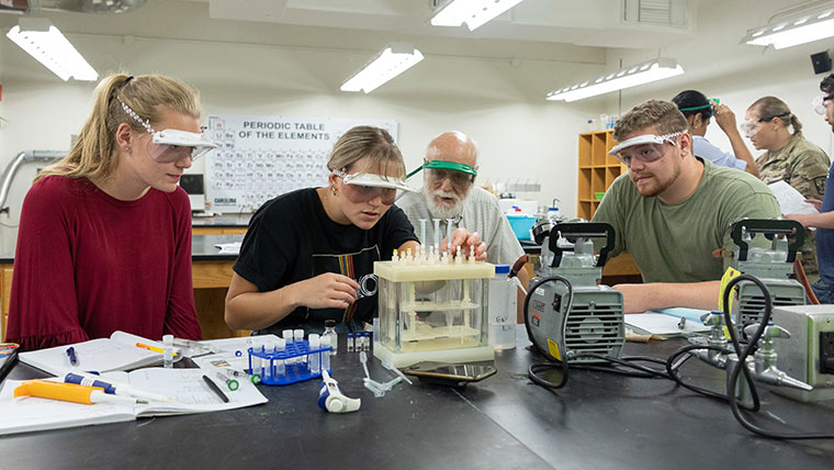 A group of chemistry students do prep work as a professor looks on.