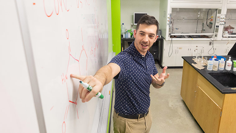 A chemistry teacher points to a dry erase board as he teaches class.
