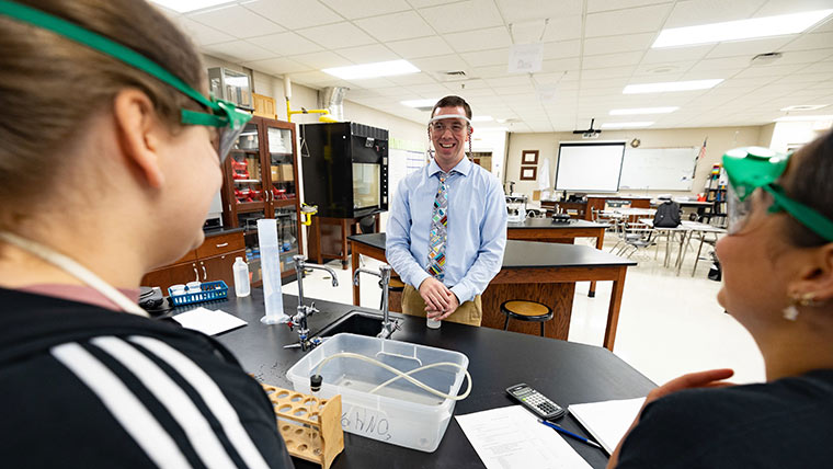 A high school chemistry teacher shares a laugh with two students during class.