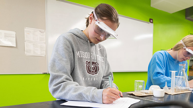 A student wearing a Missouri State hoodie takes notes during class.