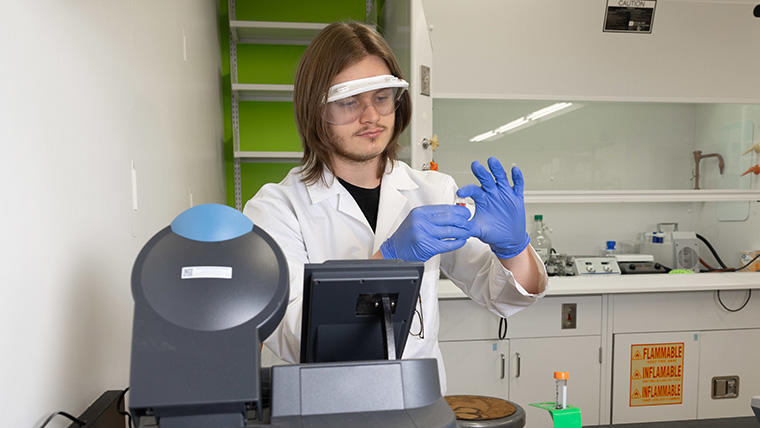 A chemistry student collects liquid samples using a machine.