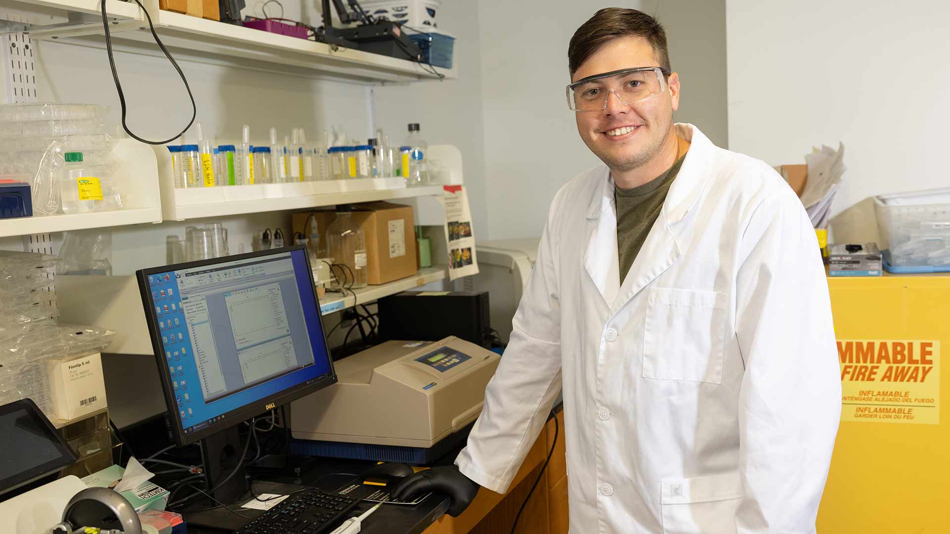 A chemistry graduate student smiles next to his workstation in a lab.