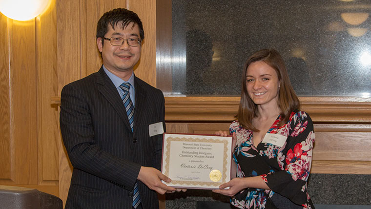 A chemistry student accepts a scholarship award from a professor during a banquet ceremony.